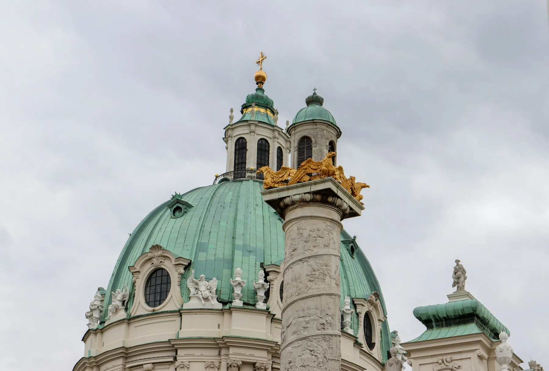 Zelená měděná kupole Karlskirche s pozlacenou lucernou a jeden ze dvou sloupů obtočených reliéfy vedle ní