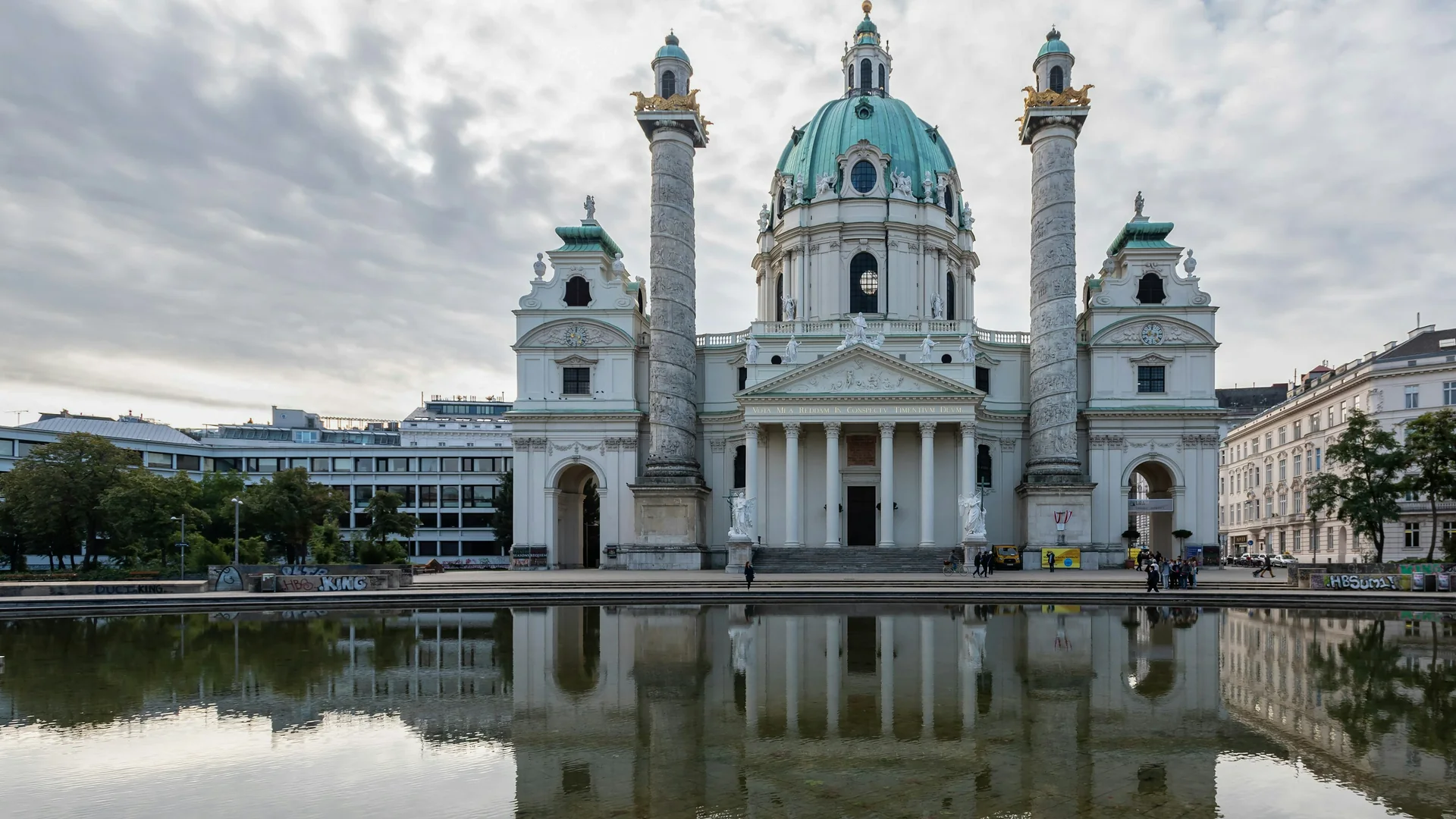 Karlskirche a její dva reliéfy obložené sloupy přes odrazový bazén na Karlsplatzu pod jemnou šedou oblohou
