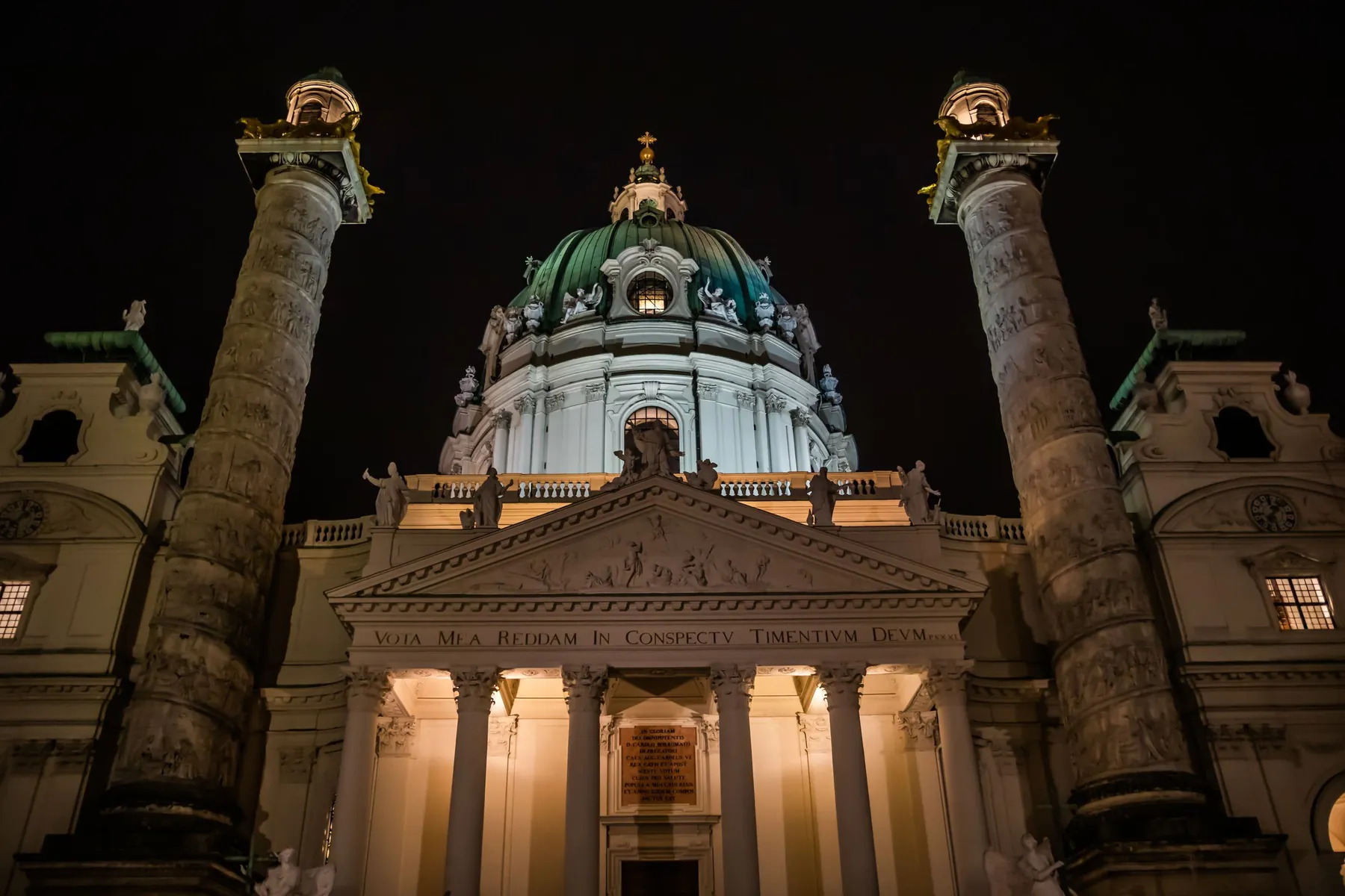 Karlskirche v noci září, její portikus se rozsvěcí mezi dvěma vysokými sloupy pod zelenou kupolí
